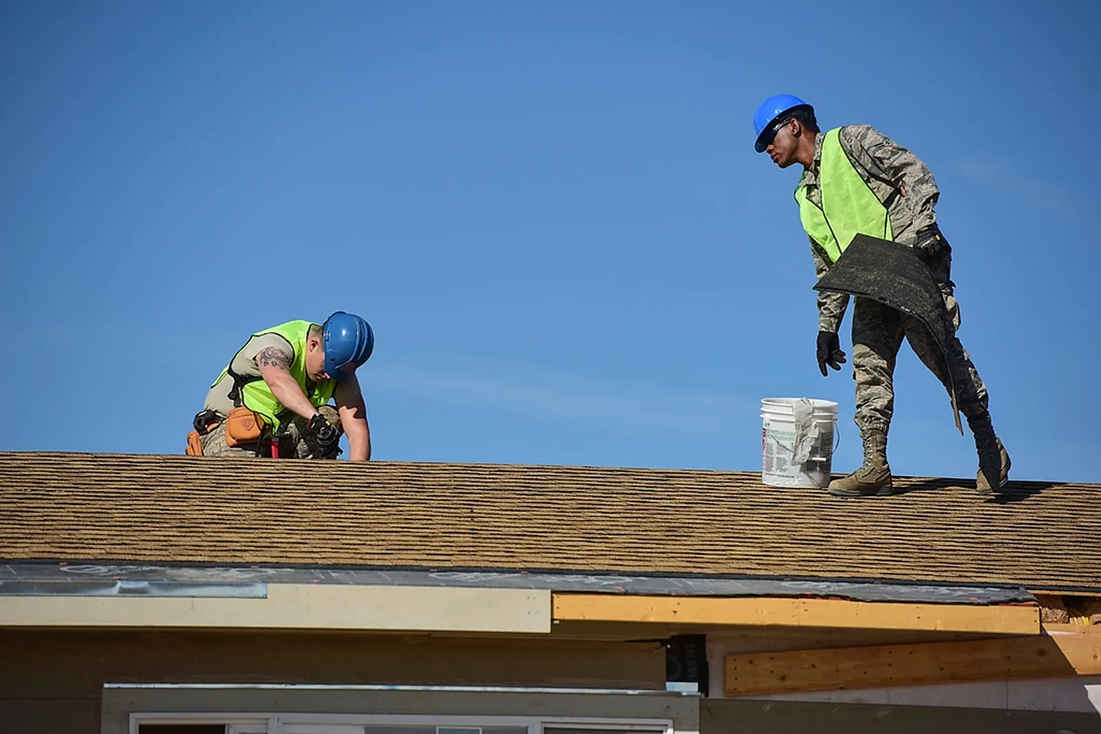 Dachdecker mit Schutzhelm und Warnweste bei der Arbeit am Dach